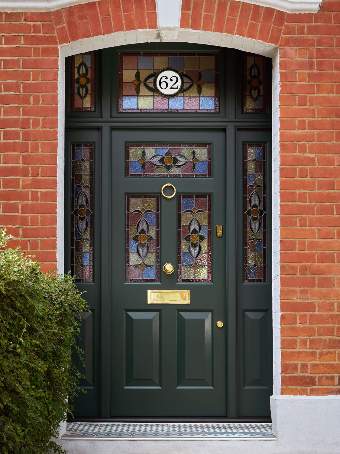 Dark green Edwardian front door with intricate stained glass panels and polished brass hardware, painted in 'Night Forest' shade, complementing a red brick exterior