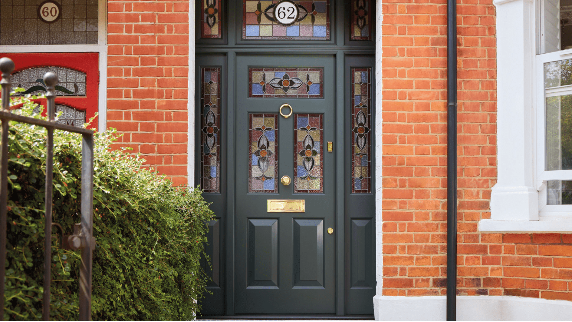 Dark green Edwardian front door with intricate stained glass panels and polished brass hardware, painted in 'Night Forest' shade, complementing a red brick exterior.